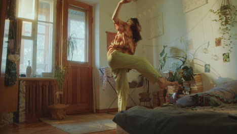 relaxed young woman in headphones dancing in sunlit cozy bedroom