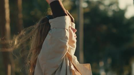 woman runs hands through hair listening to music, sunset glow on face, side shot