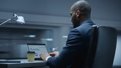 360 degree office: handsome successful black businessman sitting at desk using laptop computer. african american entrepreneur in suit working with stock market investing. moving around tracking shot