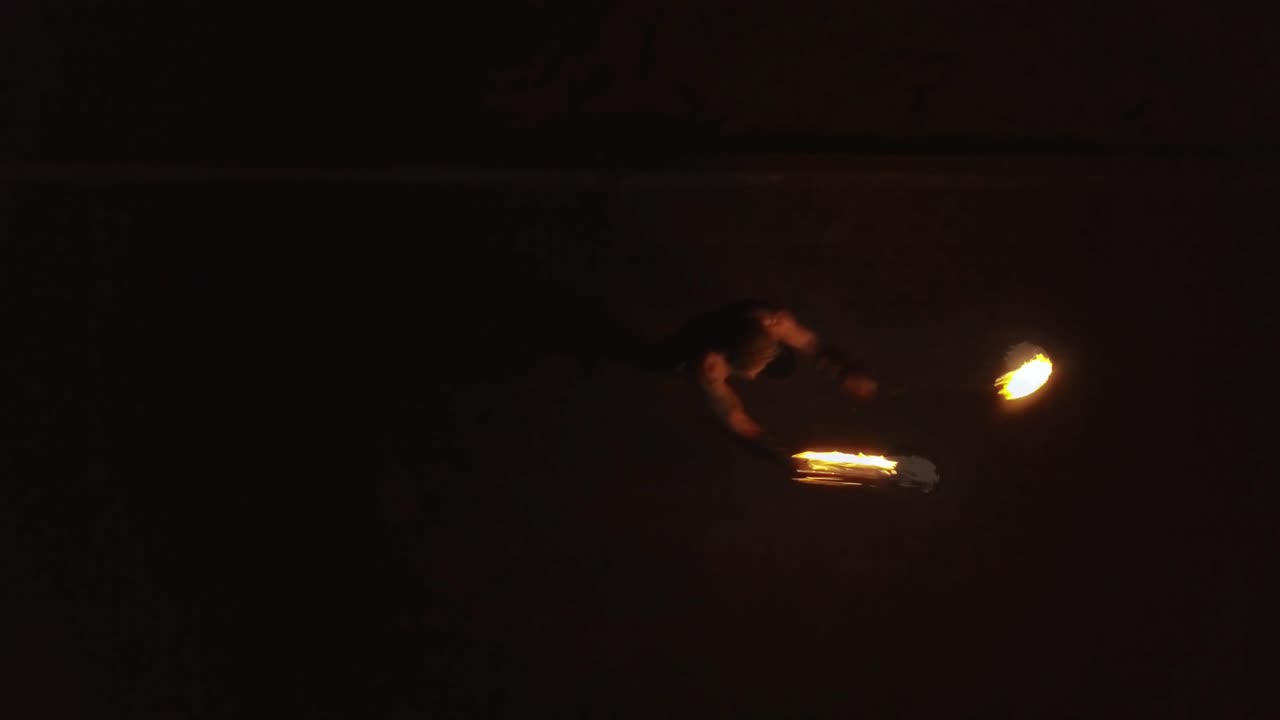 Young blond male does fire dance with two torches spins burning torches Aerial