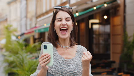 mujer feliz usar teléfono inteligente móvil celebrando ganar buen mensaje noticias al aire libre en la calle de la ciudad urbana