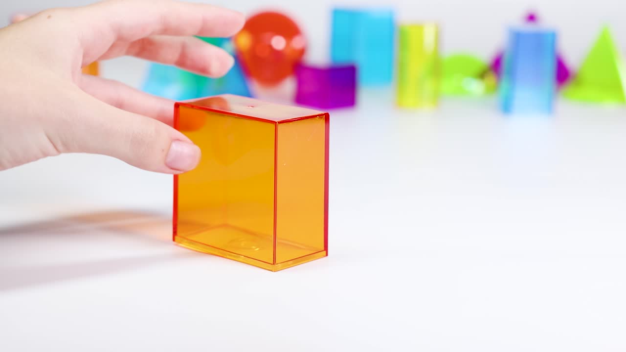 A hand interacts with vibrant 3D geometric shapes on a white surface, highlighting educational and playful elements