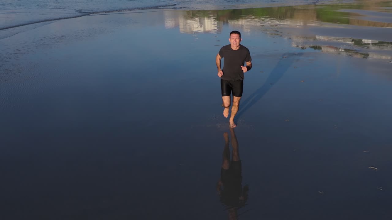 A Man Running On The Wet Sand On The Shore With Reflections. Slow Motion Shot