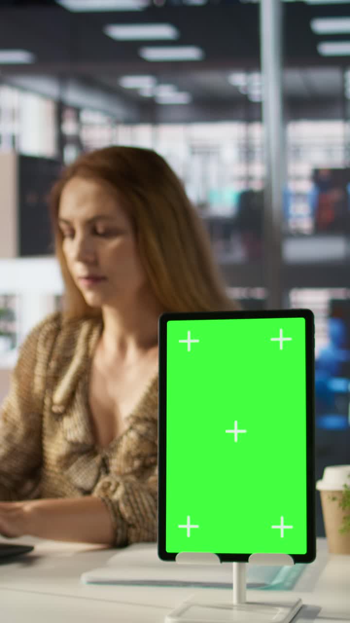 Tablet verticale con schermo verde su una scrivania in ufficio con una donna che lavora
