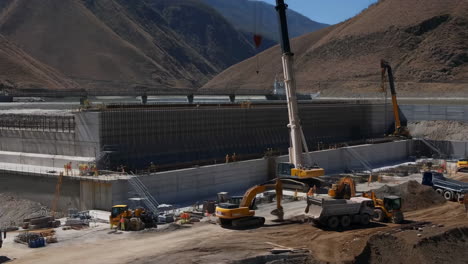large-scale dam construction site with heavy machinery and workers in a mountainous region