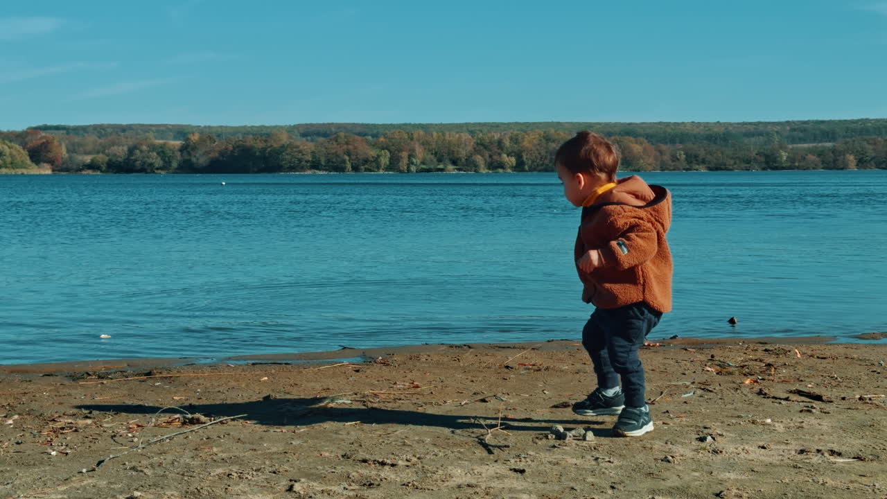 Active kid having fun time on the river bank. Baby boy is busy with throwing stones into water.