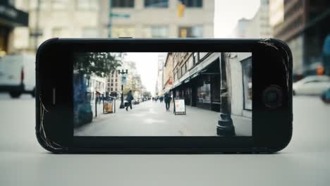 pedestrians stroll through a busy urban street as city life unfolds. the atmosphere is lively with people going about their day. a close-up of a phone showcases this vibrant scene.