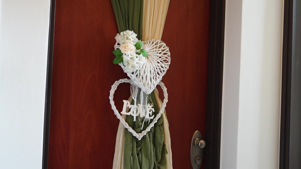 Una porta viene decorata con una ghirlanda a forma di cuore fatta di ramoscelli e fiori. La ghirlanda presenta la parola Amore e aggiunge un bel tocco per accogliere gli ospiti