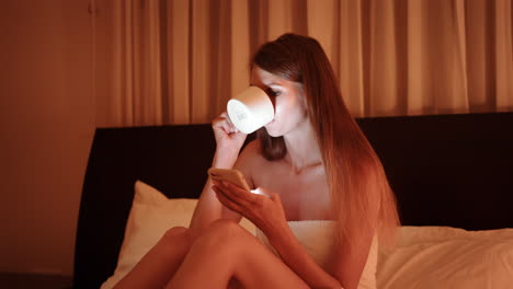 woman relaxing in bed with phone and coffee at night