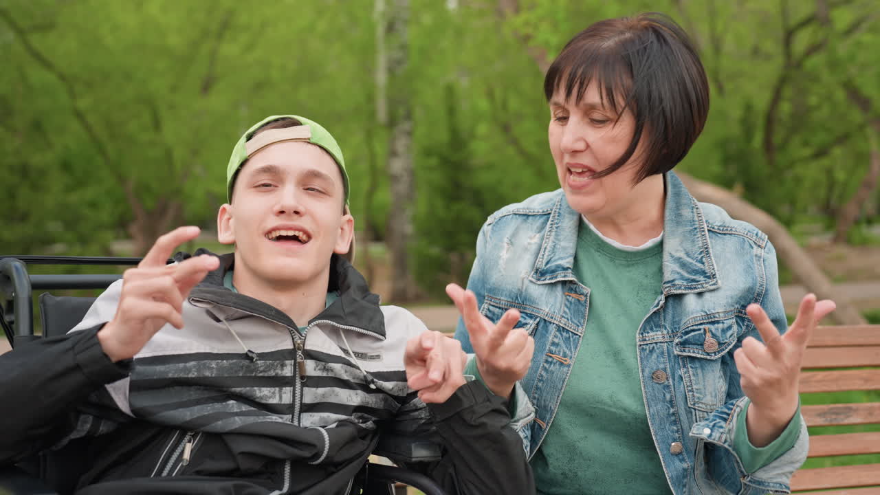 Caregiver And Young Man, Companions Communicating Joyfully Through Gestures And Happy Expressions, An Elderly Caretaker And Youthful Man Exchange Friendly Gestures And Cheerful Smiles Outdoors