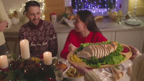 woman passing a tray with sliced bread to her friend during christmas dinner