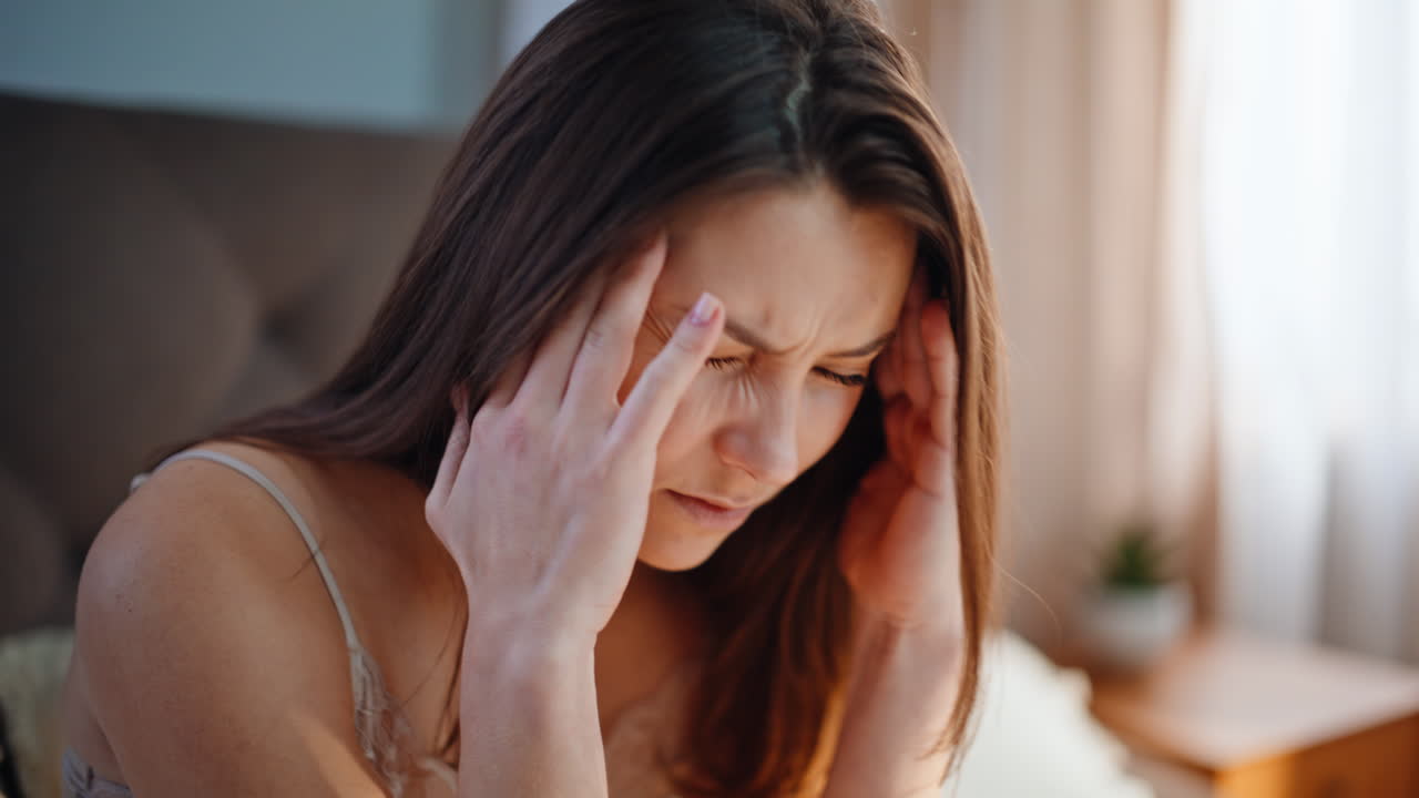 Awake girl feeling headache sitting on apartment bed closeup. Stressed woman