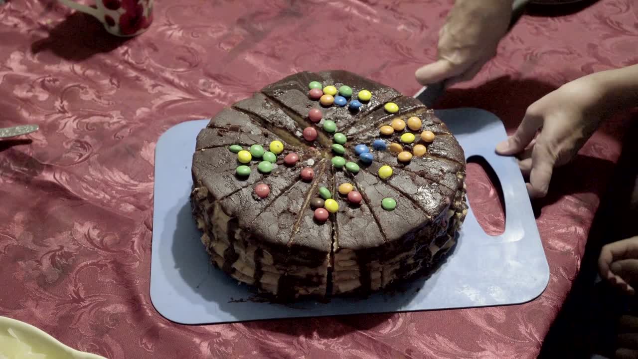 una mujer corta un pastel de chocolate en pedazos con un cuchillo grande durante unas vacaciones familiares en casa. de cerca. la vista desde la parte superior. 4k.