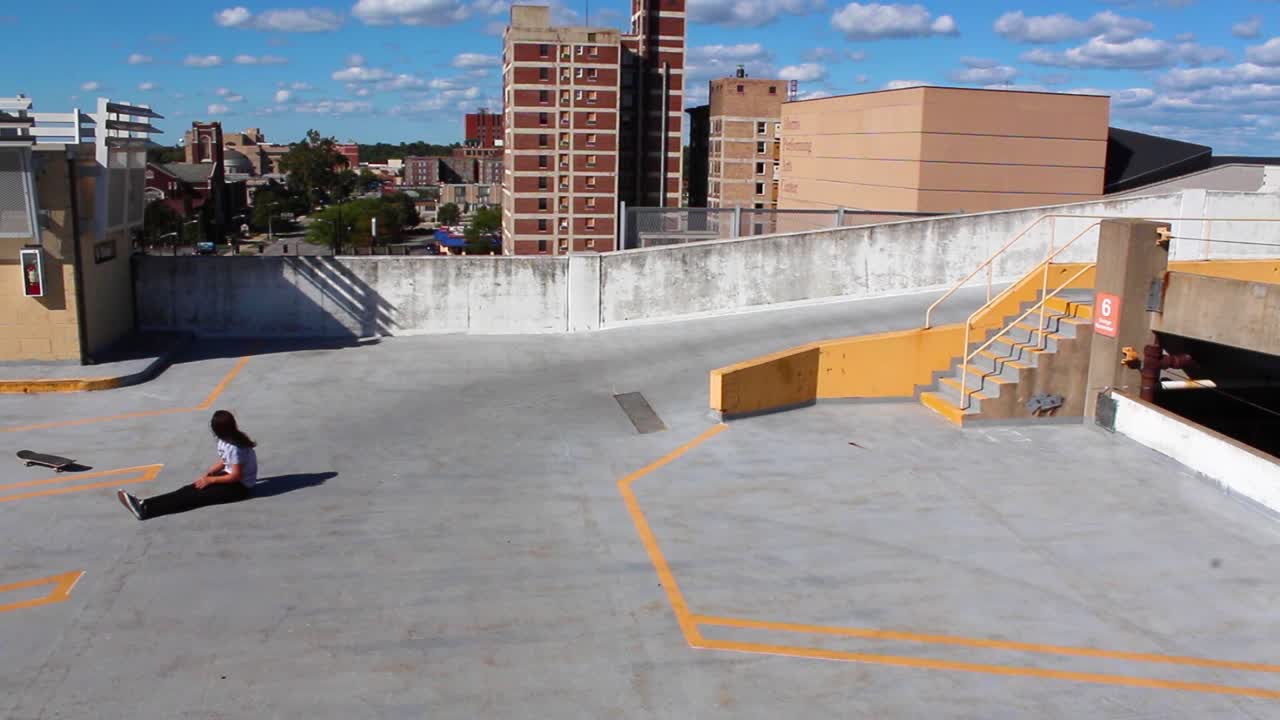 Girl skateboarding on top of parking garage and falls