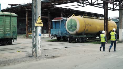 trabajadores industriales inspeccionando vagones cisterna en un patio ferroviario