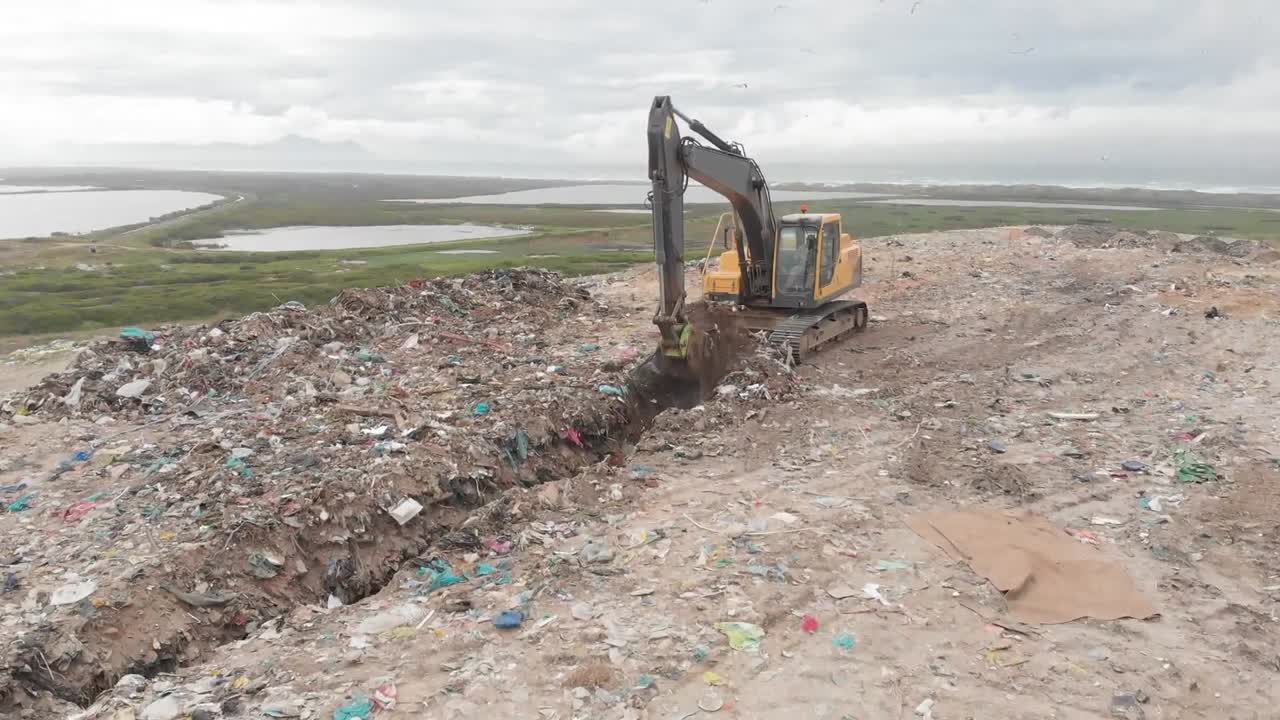 excavador limpiando basura apilada en un vertedero lleno de basura