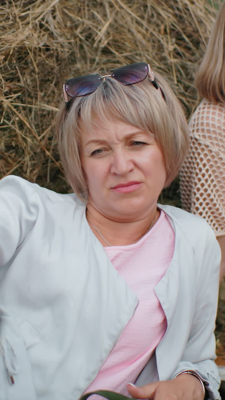 한 여자가 가게 개 머리를 만지며 누워있는 동안 다른 여자가 멀리서 바라보고, 시골의 풀 근처의 평화로운 야외 순간, 휴식을 잡고