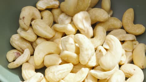 overview of dried cashew nuts tumbling in slow motion into bowl outside in sunlight - 4k food clip