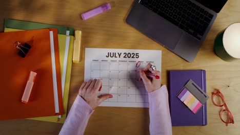 person marking dates on a july 2025 calendar