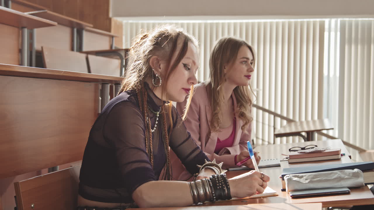 Two Female Students Taking Notes in Copybooks in Class