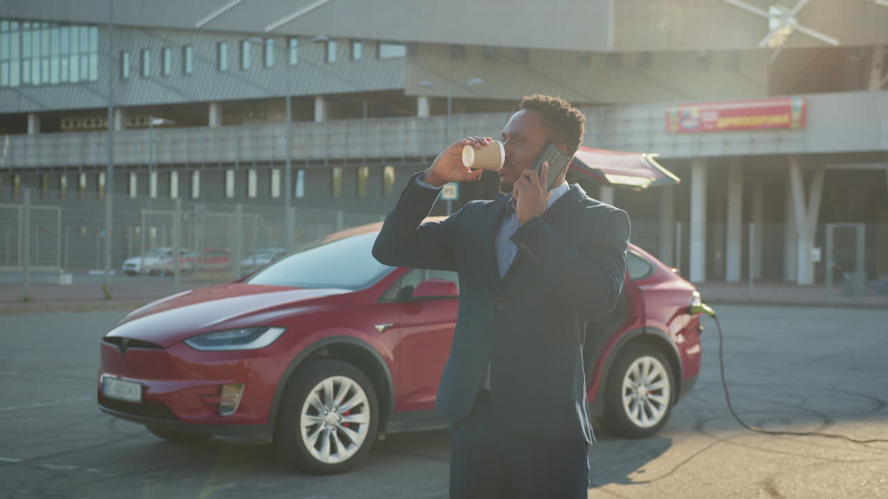 un hombre de negocios cargando un coche eléctrico y hablando por teléfono.