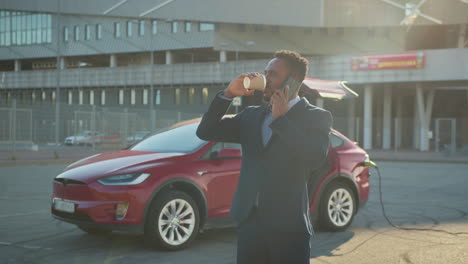 businessman charging electric car and talking on phone