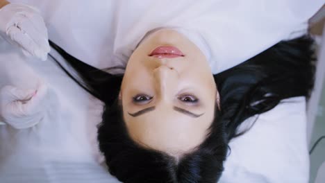 specialist dries with a sponge lips to a woman after the permanent make-up. top view of a beautiful female's face in a beauty salon. slow motion