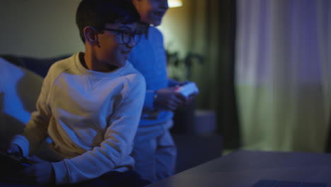 two young boys at home having fun playing with computer games console on tv fighting over controllers late at night 3