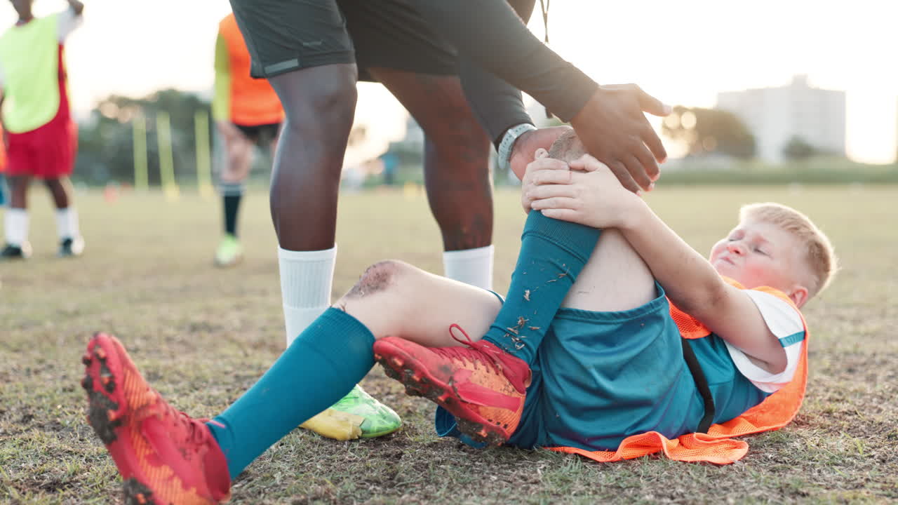 A young soccer player is injured on the field and being helped by his coach