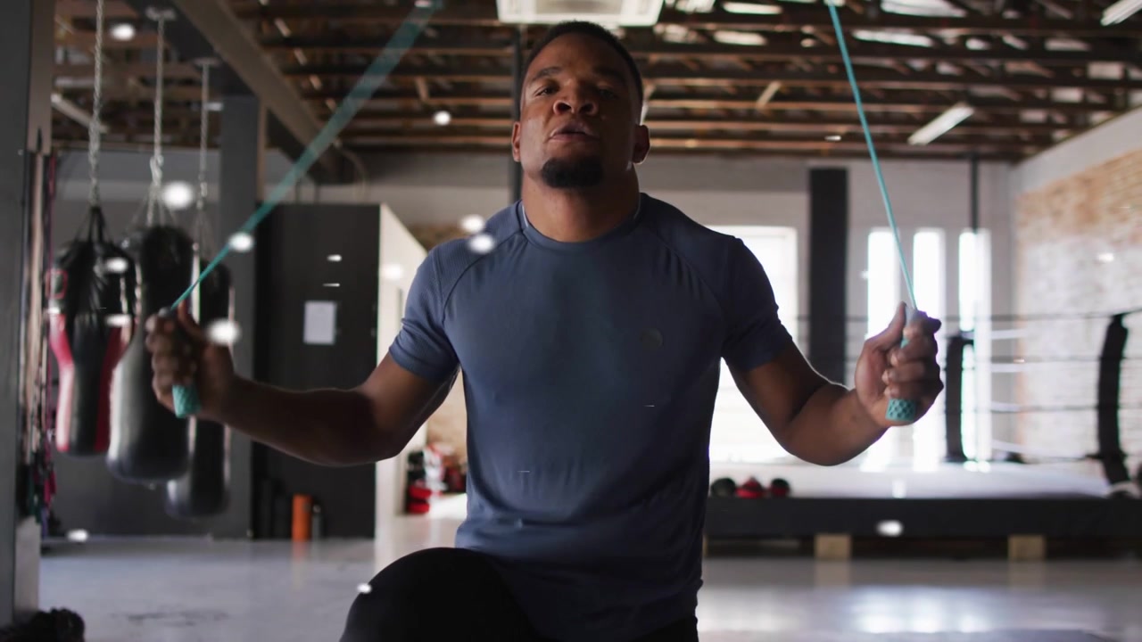 Male athlete performing high-knee steps, producing turquoise rope, training cardio in gym ring area