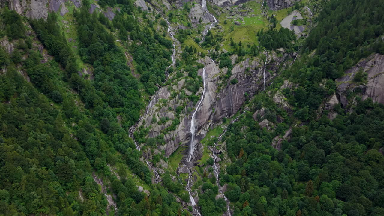 Aerial drone shot in full top-down view rising and pulling back over a waterfall surrounded by rocks and vegetation in the Swiss Alps
