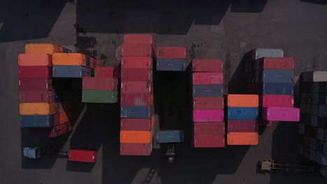 shipping containers in port with vehicles in strong morning light from top down aerial shot