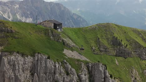 aerial view of a mountain cable car station perched on a rocky cliff surrounded by lush green slopes, with stunning mountain views in the background