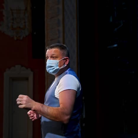 man in medical mask on scene. actor in protective mask is talking and gesticulating a lot while standing on stage in the theater. pandemic in the world