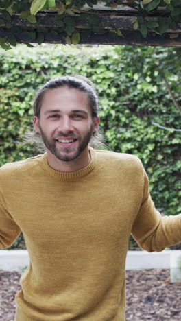 vertical video of portrait of happy caucasian man wearing yellow jumper in garden, slow motion