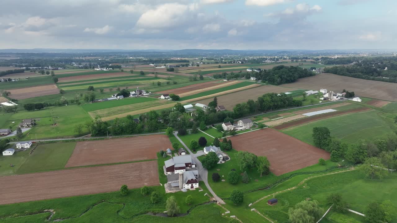 Peaceful american neighborhood with farmers houses in rural area of USA. Cloudy day in summer. Roof of houses and cars on road. Pattern of farm fields in May. Pennsylvania USA. Aerial wide shot.