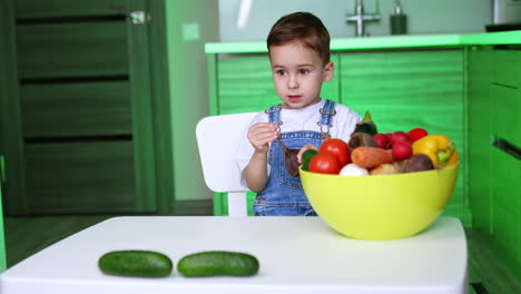 child discovers bright produce. a young child sits at a table, observing a large bowl filled with various fruits and vegetables, enjoying the moment