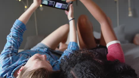 happy diverse female friends lying on bed and using tablet at home, slow motion