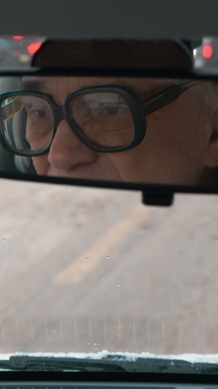 Man reflected in a car's rearview mirror driving on a snowy day