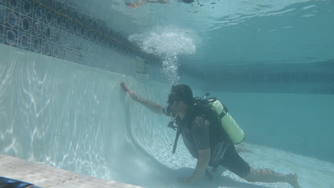 스쿠버 장비의 전문 수영장 청소부는 브러시로 수영장 옆에서 수중 먼지와 조류를 닦습니다.