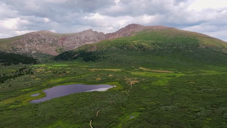 Winding-dirt-hiking-trail-path-passes-small-pond-lake-in-guanella-pass-colorado,-aerial-push-in