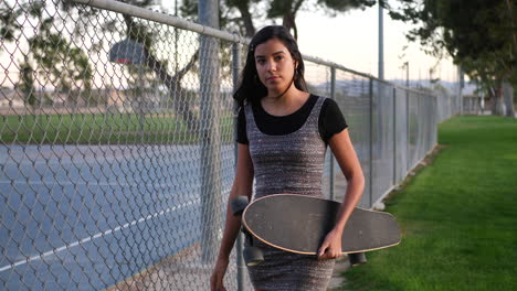 Una-Linda-Joven-Hispana-Caminando-Por-Un-Parque-Urbano-Con-Su-Patineta-A-Cámara-Lenta