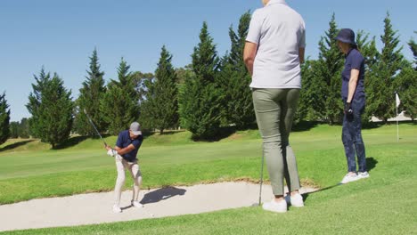 caucasian senior man hitting golf ball out of a sand trap at golf course on a bright sunny day