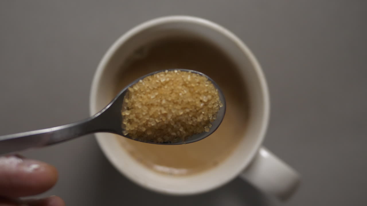 One heaping teaspoon of turbinado sugar dropped into a hot cup of light coffee, mmmm, caffeinated goodness. Slow motion 4K.