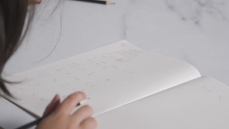 Close-Up-Shot-Of-Young-Girl-At-Table-Concentrating-On-Maths-In-School-Book-