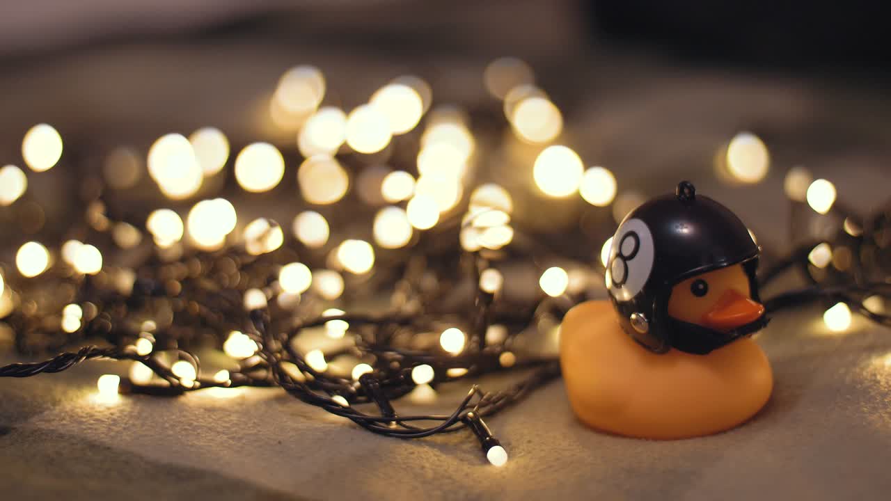 fotografía en primer plano de un pato de goma con un casco de motocicleta hecho a mano sobre el fondo de una guirnalda de navidad