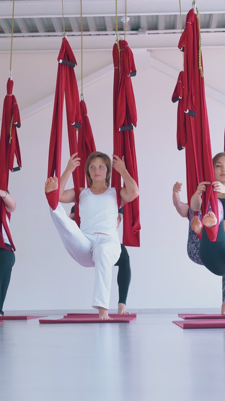 motion along women group practicing anti-gravity yoga and stretching legs with long red hammocks in light training room