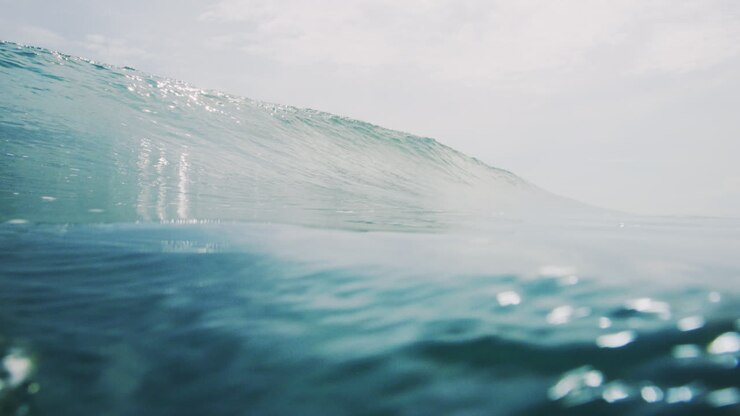 Wide low view of glistening ocean water and wave crashing on surface