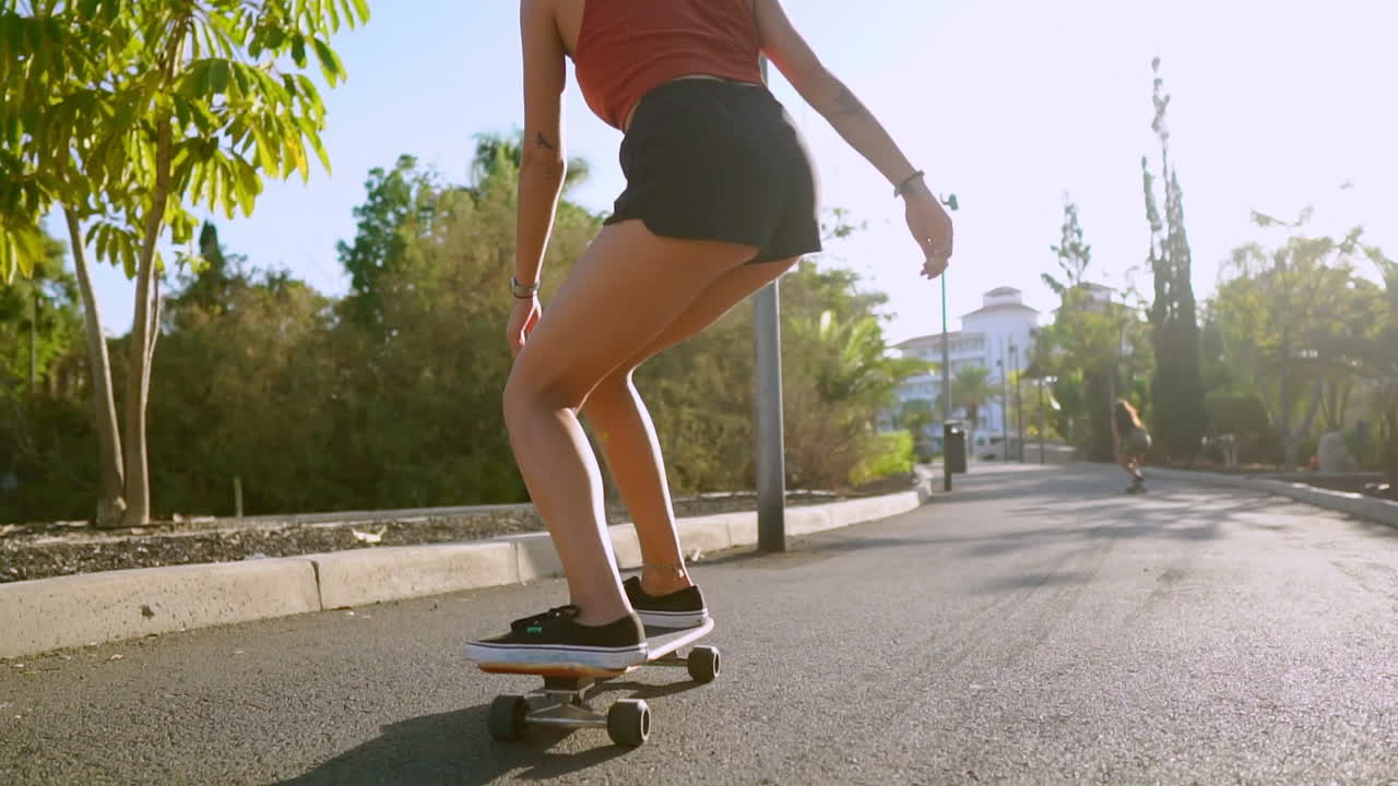 Embracing the sunset's warmth, a woman rides her skateboard along the palm-fringed park path with sand, her smile reflecting the essence of a healthy and happy lifestyle