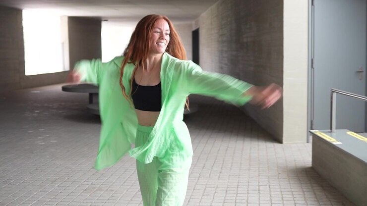 A woman is energetically dancing in a vibrant green outfit in a modern urban setting